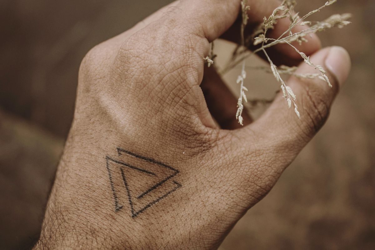 Hand with a small fine-line triangle tattoo holding dried plant stems
