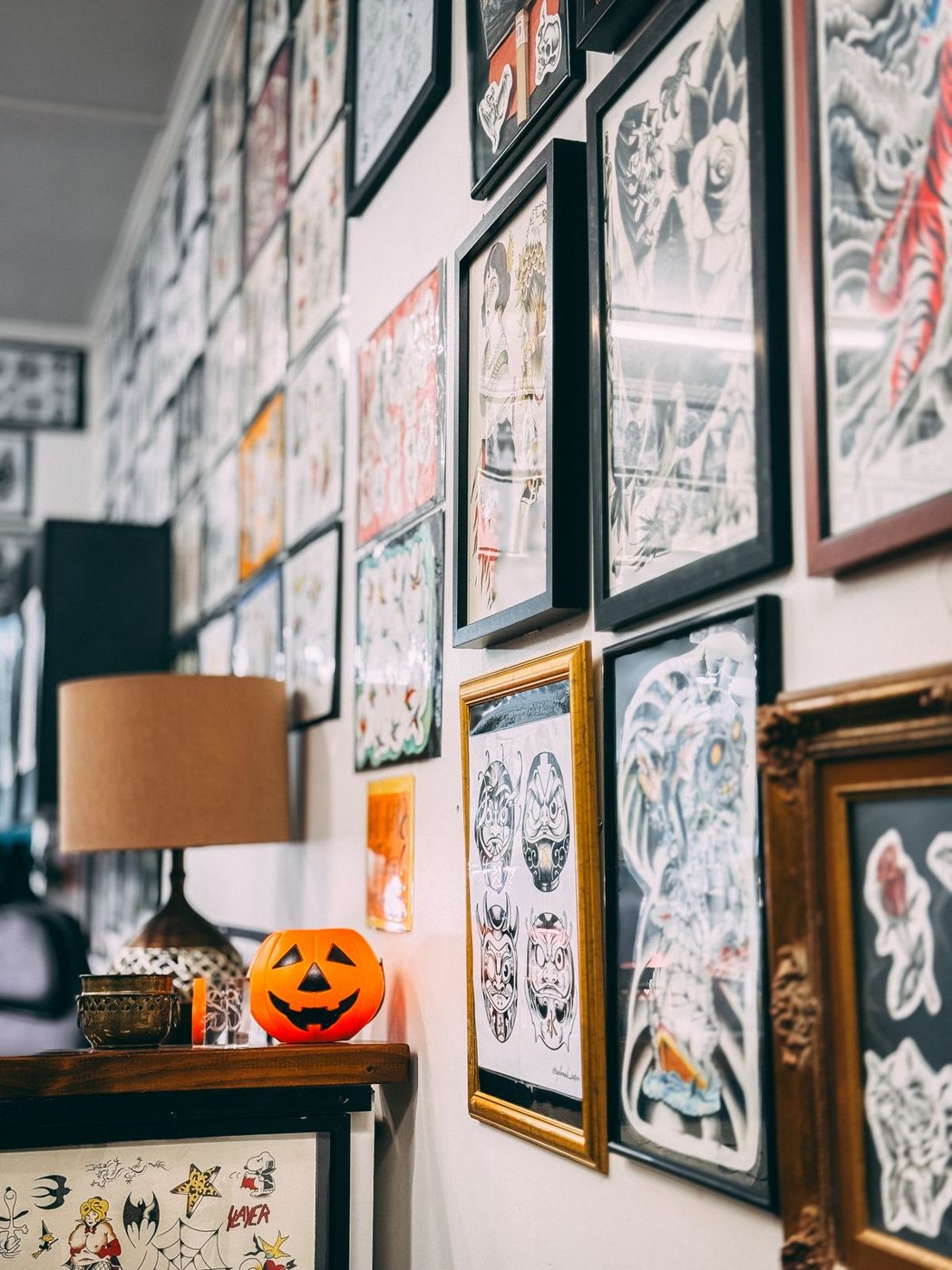 Tattoo shop wall covered with framed flash designs, with a small carved pumpkin on a lamp-lit shelf