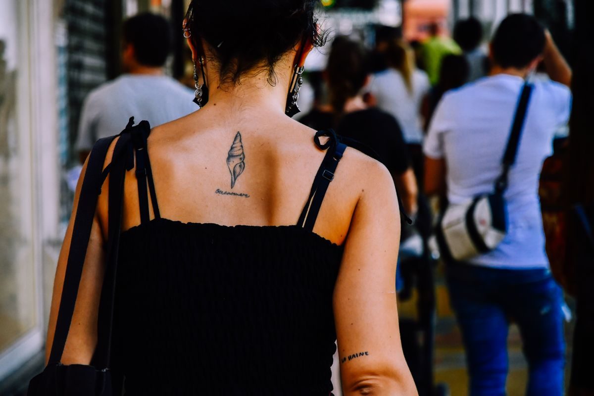 Woman seen from behind in a city crowd with a small tattoo between her shoulder blades