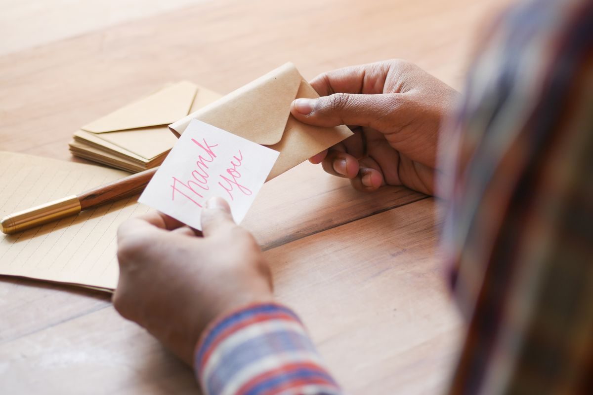 Hands holding a small handwritten thank you card next to an envelope