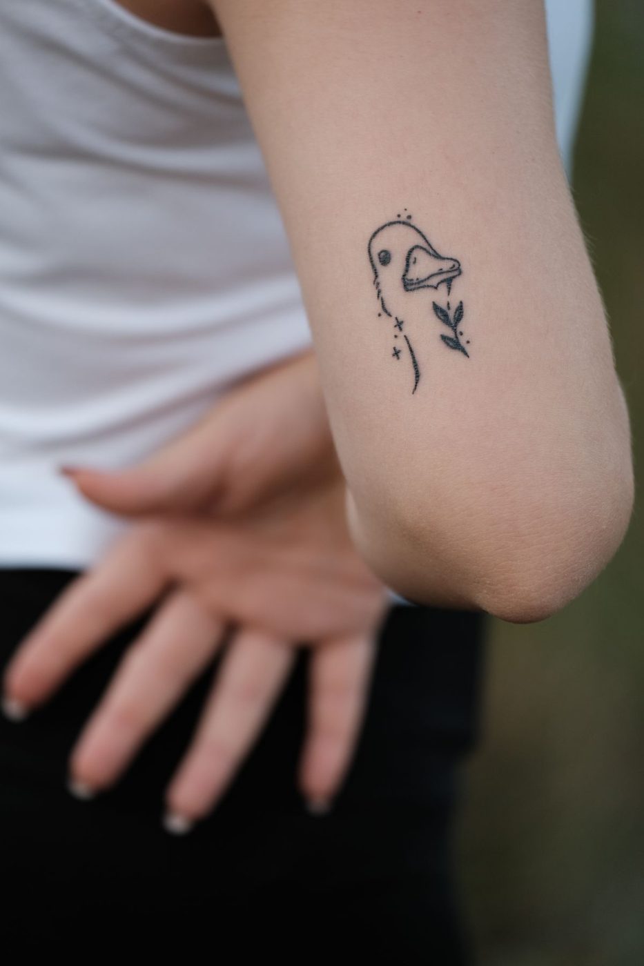 Small doodle-style bird tattoo on the back of an upper arm