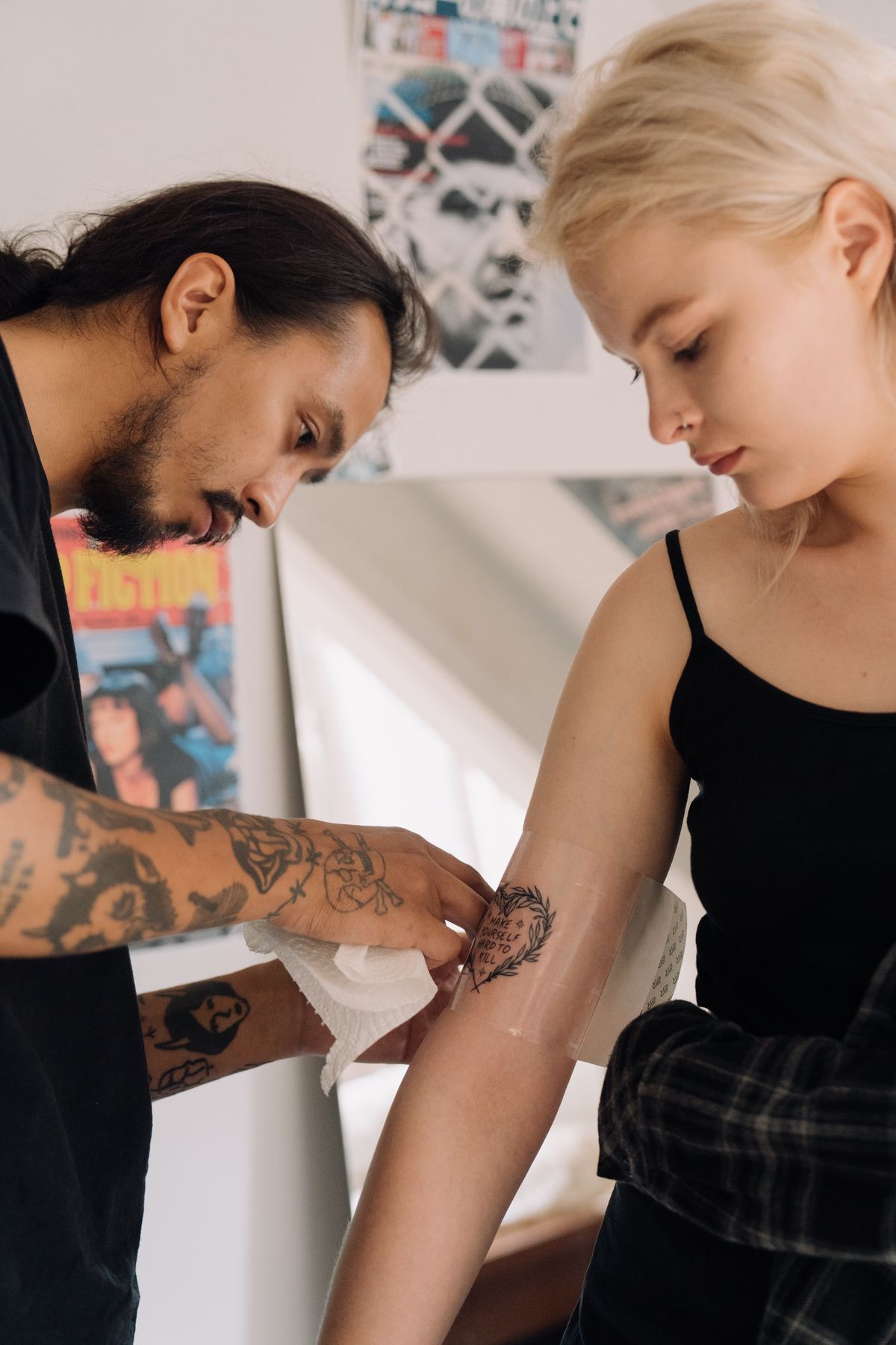 A tattoo artist applying a second-skin adhesive bandage to a client's freshly finished forearm tattoo