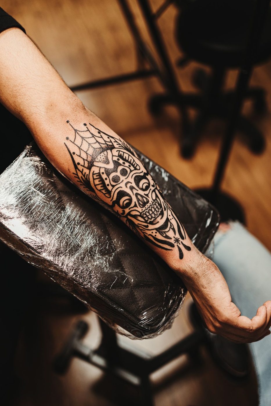 Forearm with a black ornamental tattoo of a skull with spiderweb linework