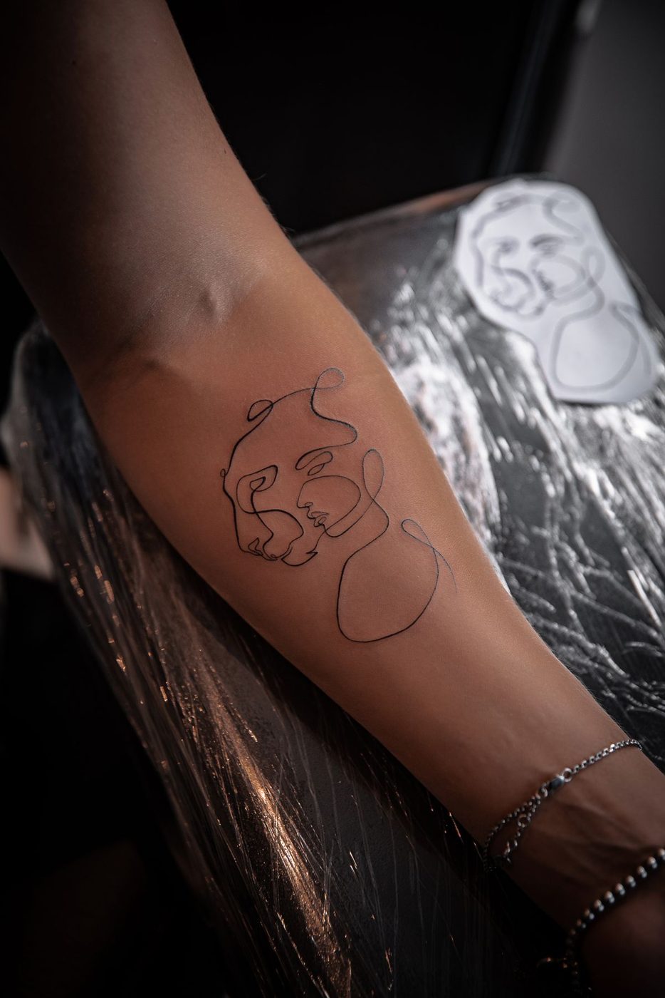 Single continuous thin-line figure tattoo on a forearm