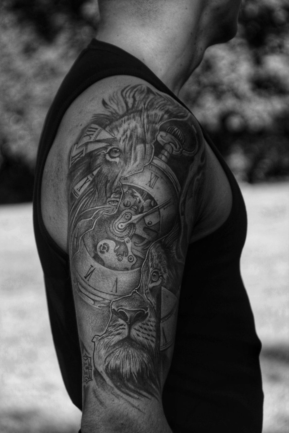 Black and grey realistic tattoo of a lion and clock gears on an upper arm
