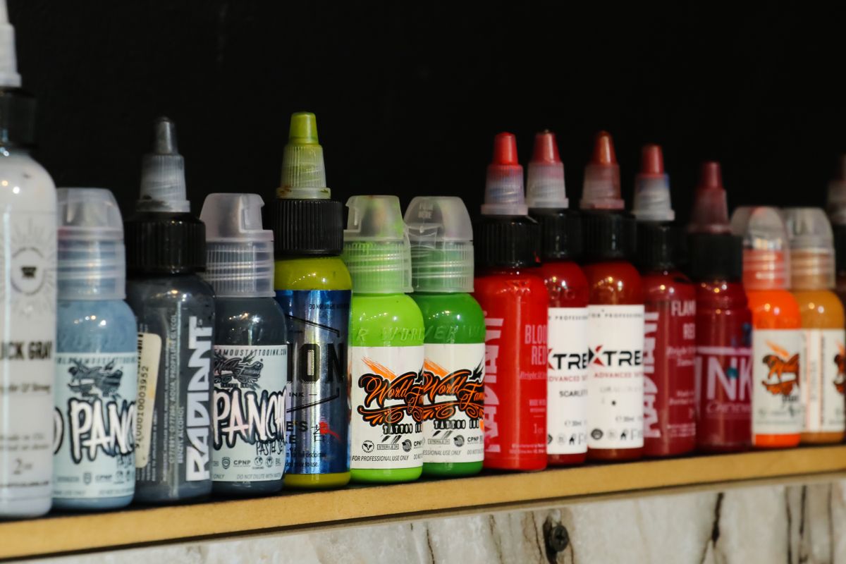 A shelf of tattoo ink bottles from various brands, including World Famous Ink, lined up in a tattoo studio